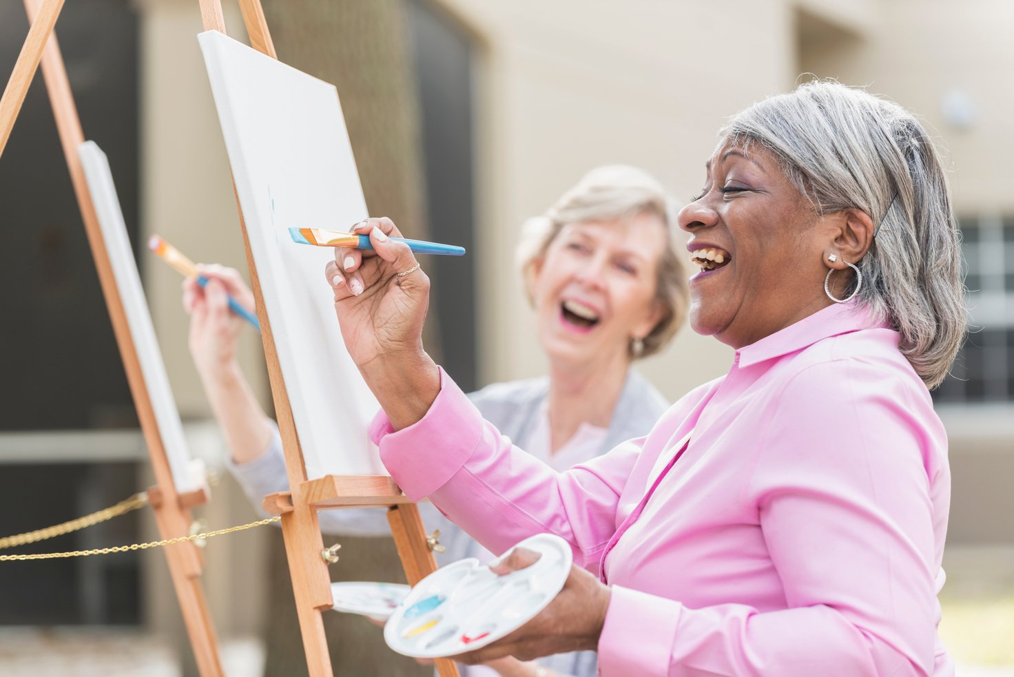 Two senior women having fun painting in art class